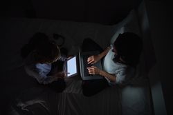 Mother with son browsing gadgets while doing homework in darknes
