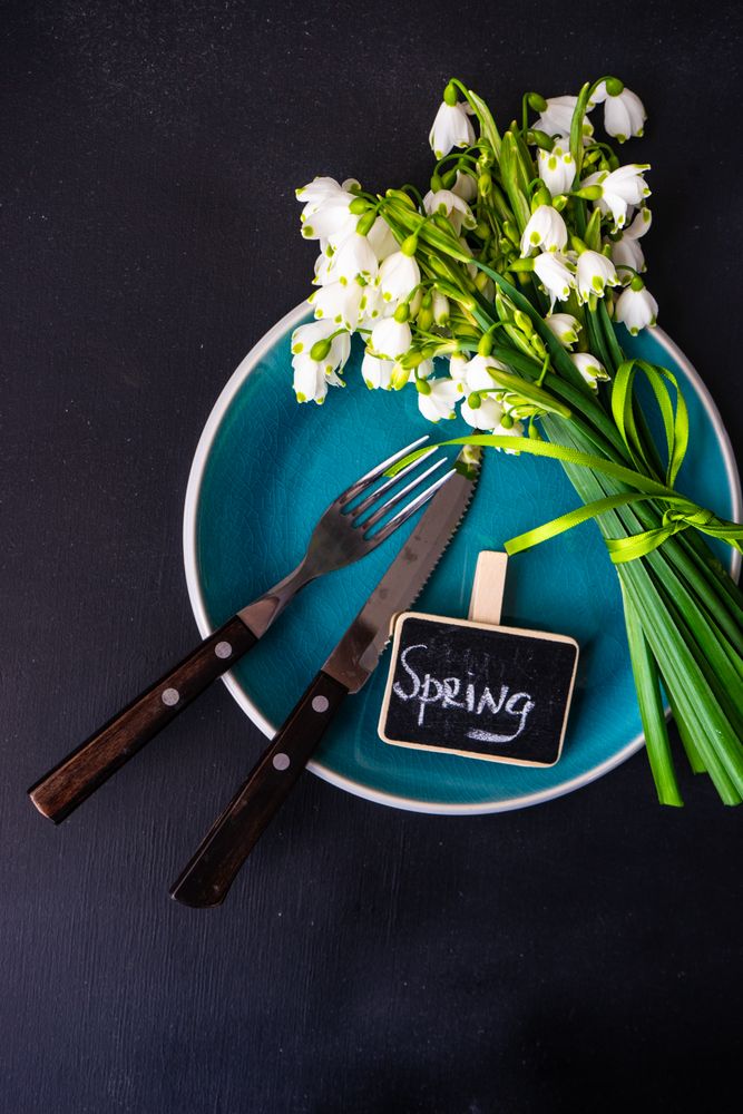 Top view of table setting for spring dinner with flowers on teal plate