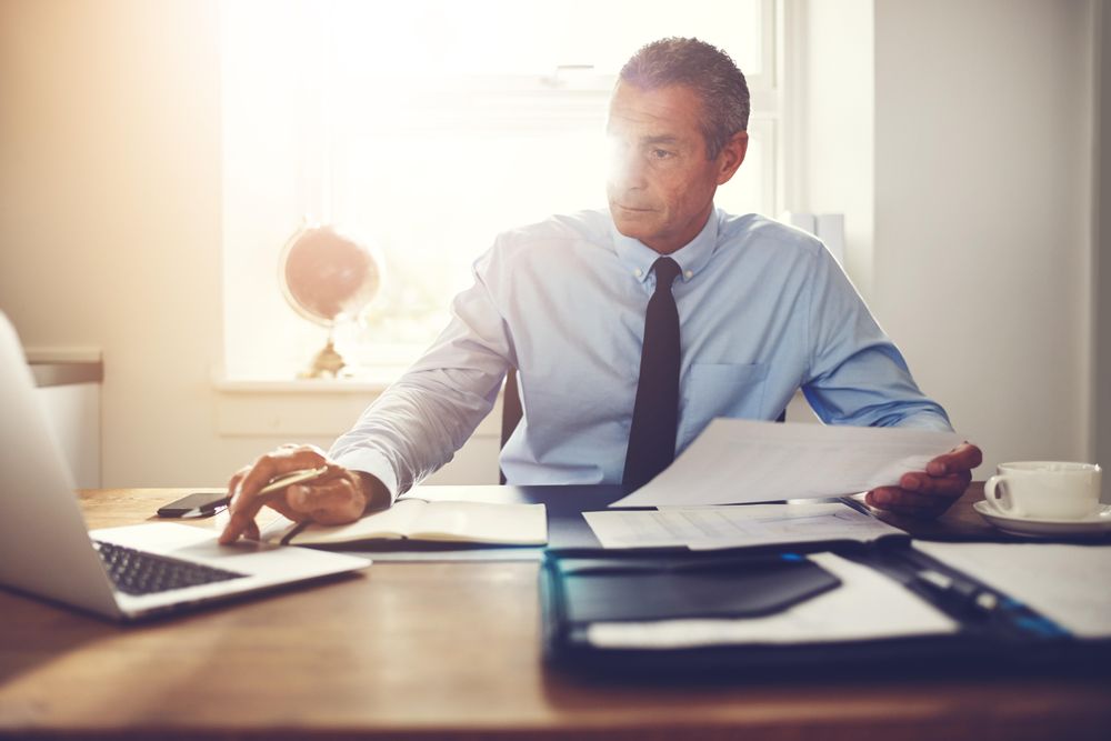 Man in business attire working at his laptop with pen in hand