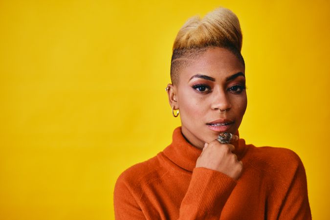 Studio shot of serious Black woman with short blonde hair in orange sweater