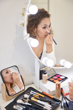 Young woman applying makeup on eyes looking at mirror