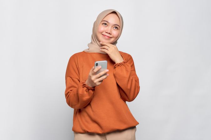 Calm and happy Muslim woman holding her smartphone and looking up
