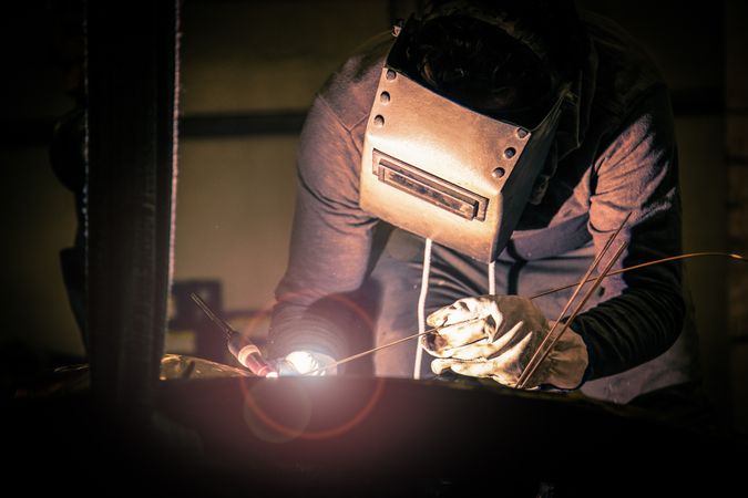 Man in mask welding metal ware in darkness