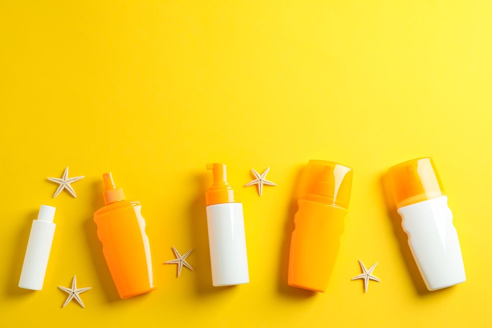 Flat lay composition with sunscreen sprays and starfishes on color background, space for text. Summer vacation backdrop
