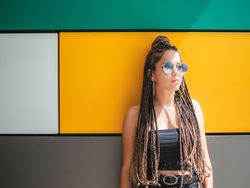 Charming teenage girl with dreadlocks in sunglasses nearby colorful wall