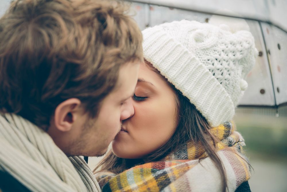 Affectionate couple kissing under umbrella on cold day