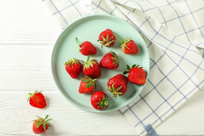 Plate with fresh strawberries and kitchen towel on bright wooden background, top view and space for text