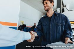 Young auto mechanic shaking hands with satisfied customer in garage 5rl11b