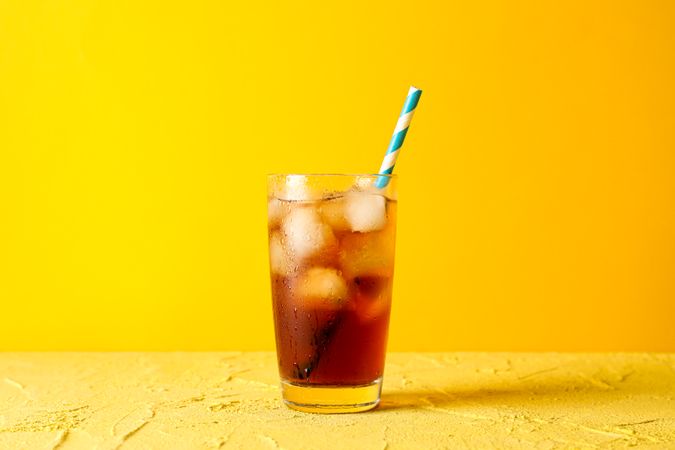 Glass with cold cola and tubule against yellow background