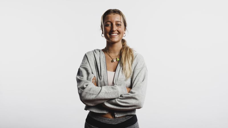 Portrait of smiling fitness woman standing against light background with arms crossed