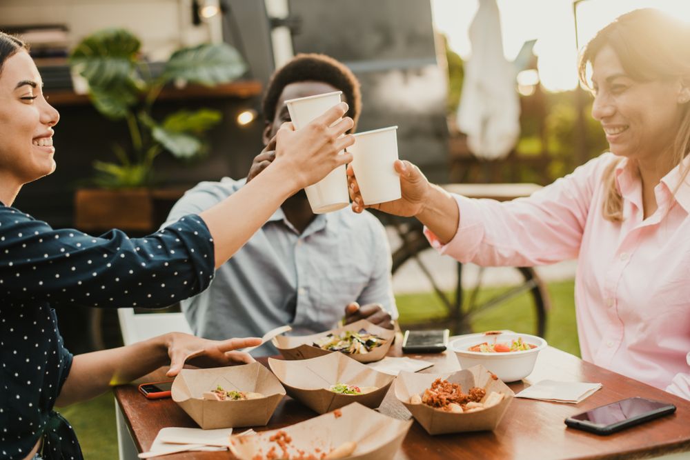 Happy people eating and cheering at food truck restaurant - Focus on girl hand holding cup of drink