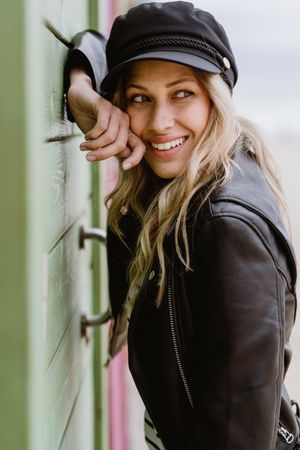 Stylish woman smiling and leaning on bright wooden cabins on beach