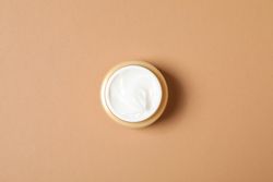 Cream jar on orange background, top view