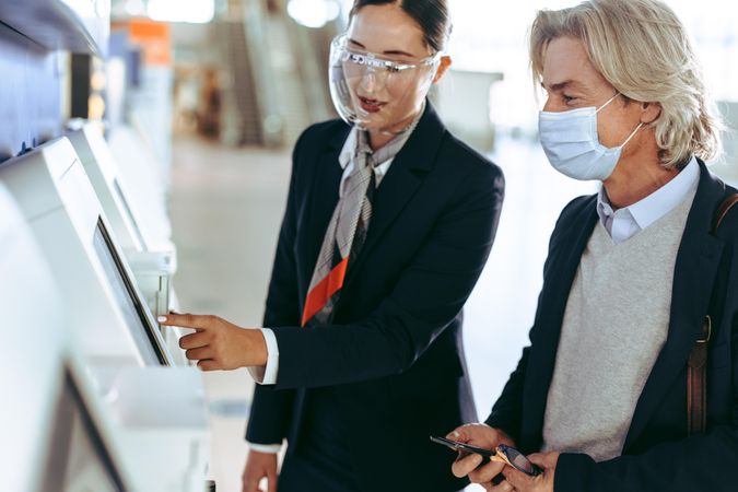 Man in facemask at self check out kiosk with airport staff