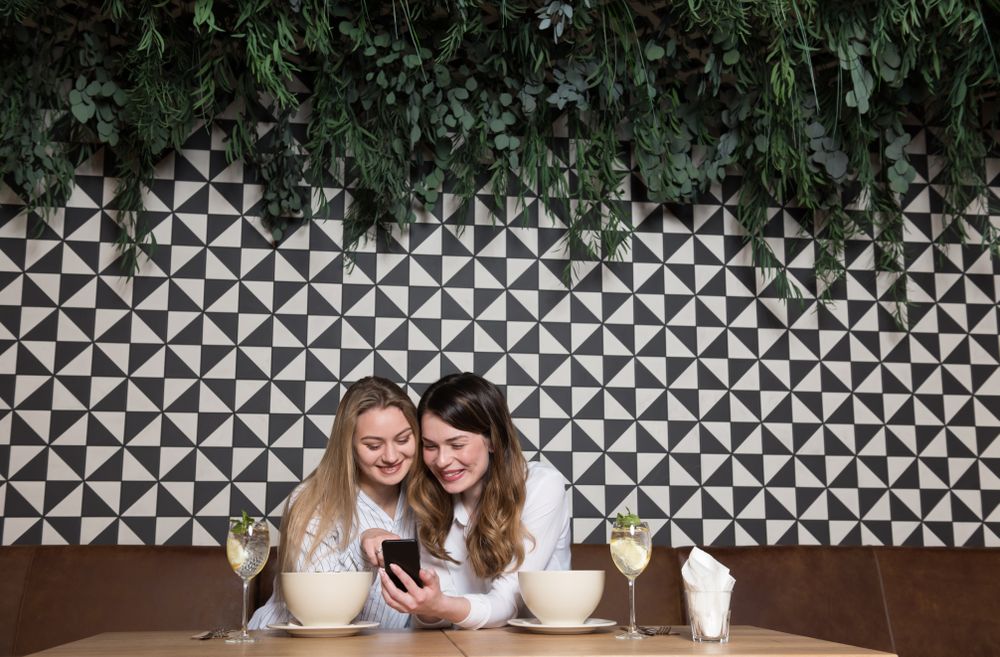 Women friends using smartphone at restaurant table