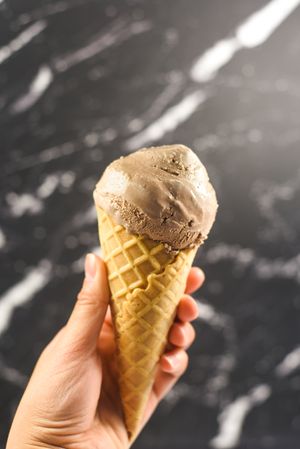 Hand holding chocolate ice cream cone on marble background
