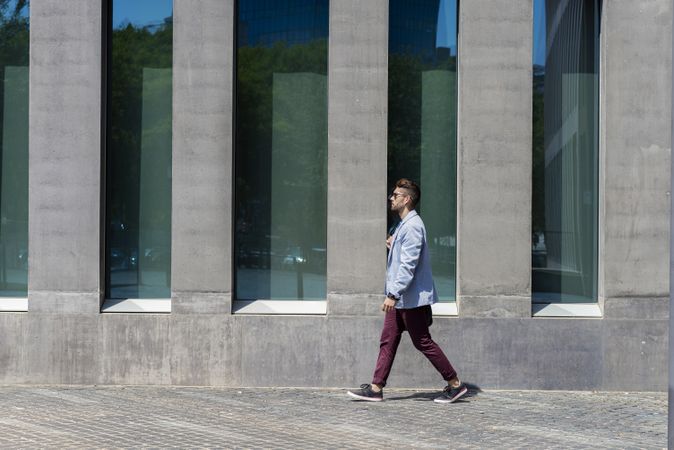 Side view of man walking in the sun outside of building