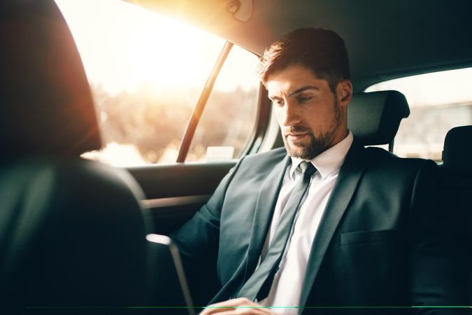 Handsome businessman using laptop while sitting on back seat of a car