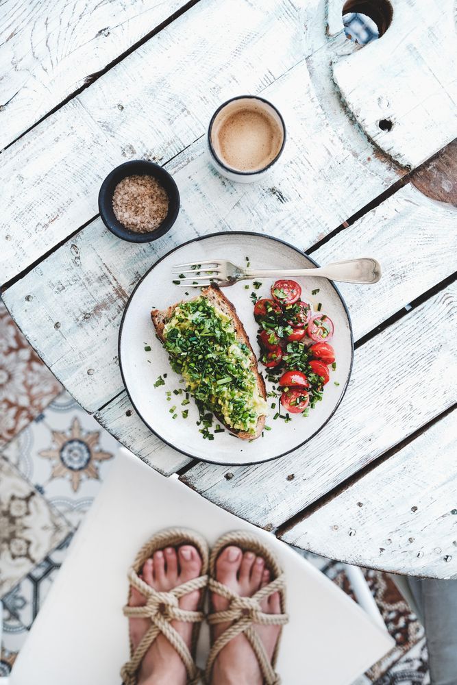 Avocado toast on sourdough bread, cherry tomatoes, coffee, with feet, on light background
