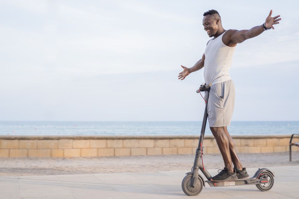Cool adult Black man riding scooter in street