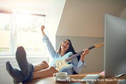 Happy female playing guitar at her desk bDBdp5