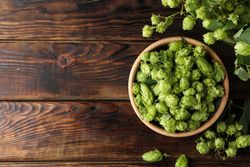 Wooden bowl and glass jar with hop on wood background, top view