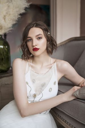 woman with red lips in white dress looking at camera while sitting on floor beside sofa