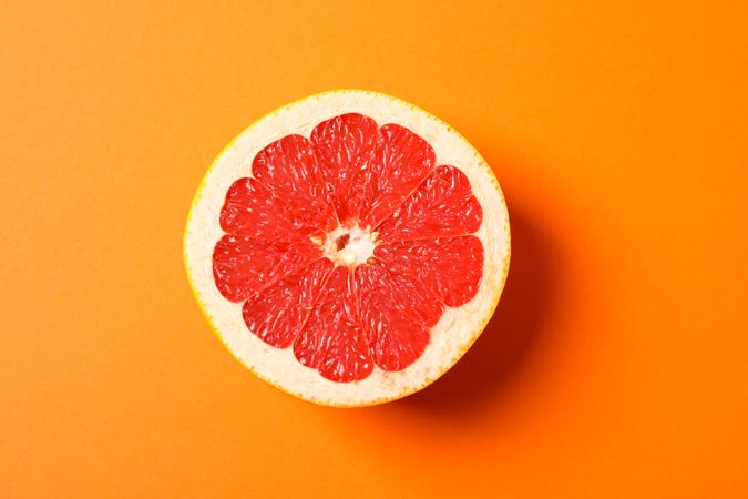 Grapefruit slice on orange background, space for text