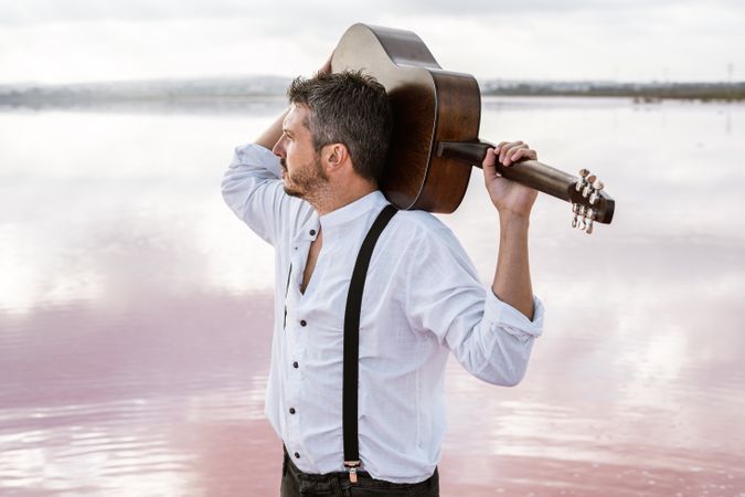 Musician gazing and carrying guitar behind back while standing on beach