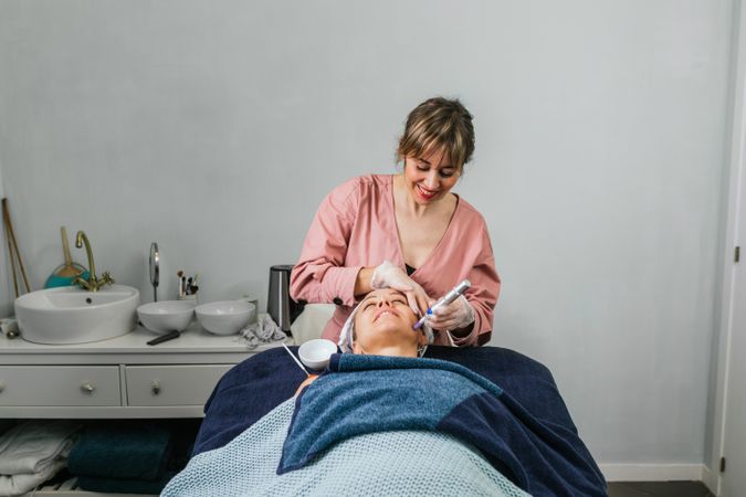 Cosmetologist doing microdermabrasion procedure of face of client
