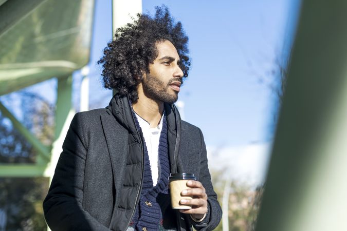Black man in jacket holding beverage while looking in the distance
