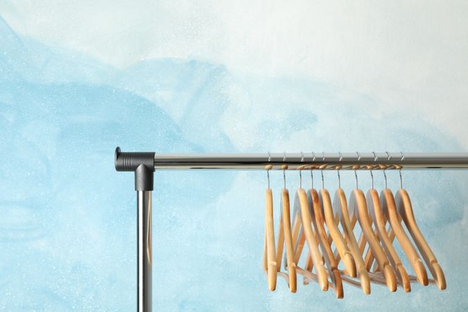 Hangers on rod against blue background, space for text