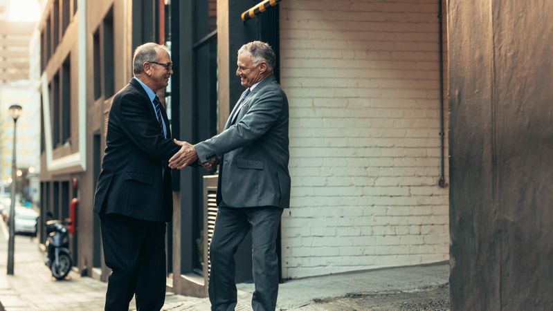 Mature business professionals giving handshake standing outdoors