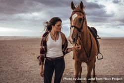Portrait of woman leading her   horse on the beach with storm clouds 5ogE15