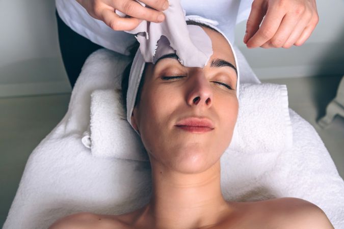 Beautician's hands removing facial mask from woman
