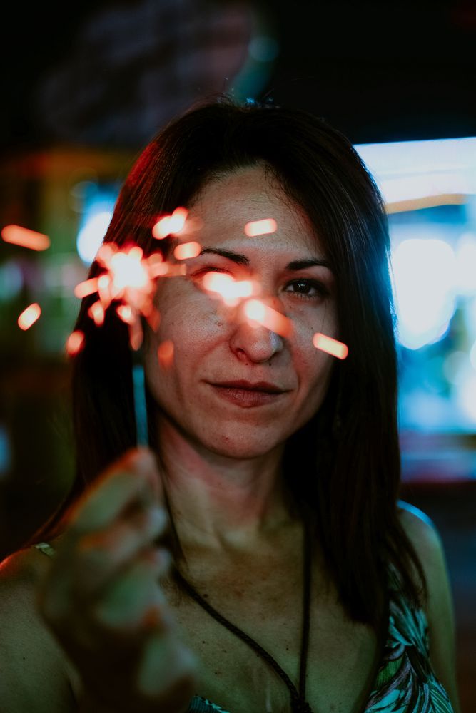 Woman holding sparkler on fairground in evening