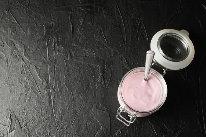 Glass jar with fruit yogurt on dark cement background, space for text