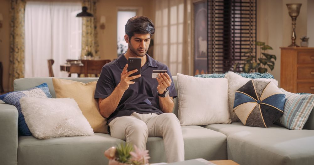 Indian Man Using Credit Card and Smartphone for Online Shopping at Home.