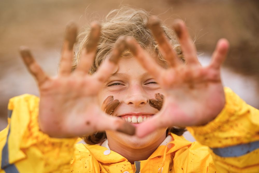 Smiling boy with dirty face looking at camera through fingers