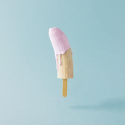 Banana with ice cream stick and pink syrup on pastel blue background