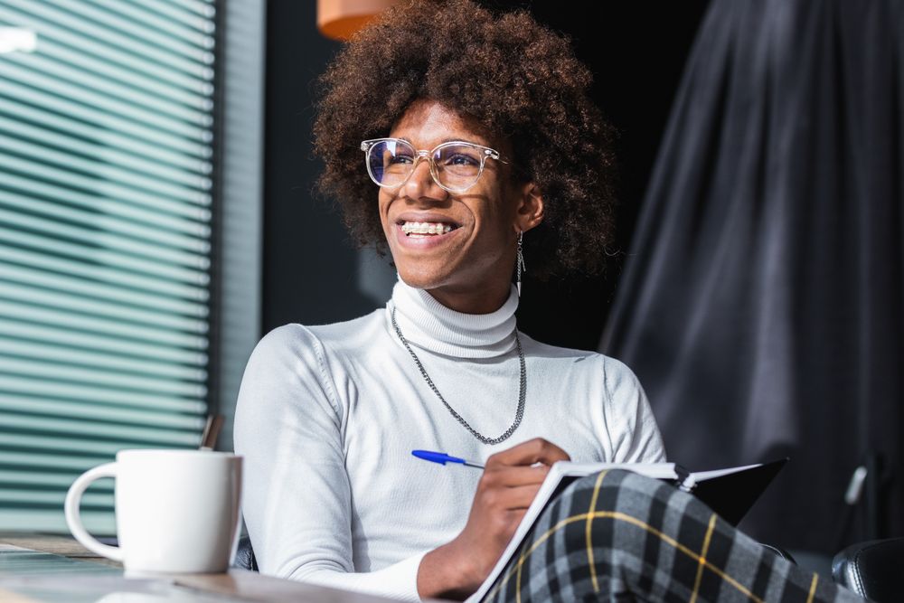 Happy trendy young Black guy doing assignment in cafe