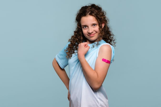 Girl flexing arm with pink bandage after receiving vaccine shot.