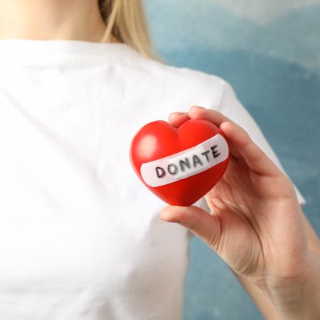 Woman holds heart on blue background, close up. Health care, organ donation