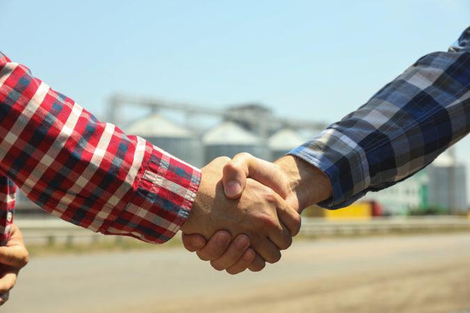 Businessmen shake hands against silos. Agriculture business