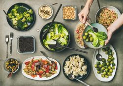 Vegan dinner table setting of healthy dishes in plates on table with woman’ hands