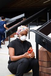 Woman nurse in PPE checks mobile phone while sitting on steps on break