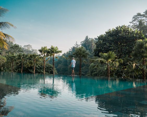 Man standing beside swimming pool surrounded by tropical trees