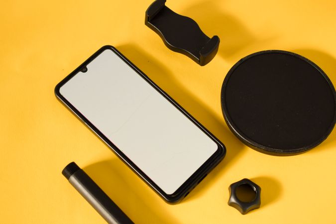 Mock up phone and accessories scattered on yellow table with shadow and space for text