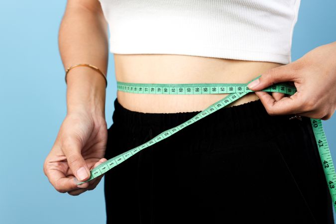 Slim Asian Young Woman Measuring Her Waist using Measuring Tape