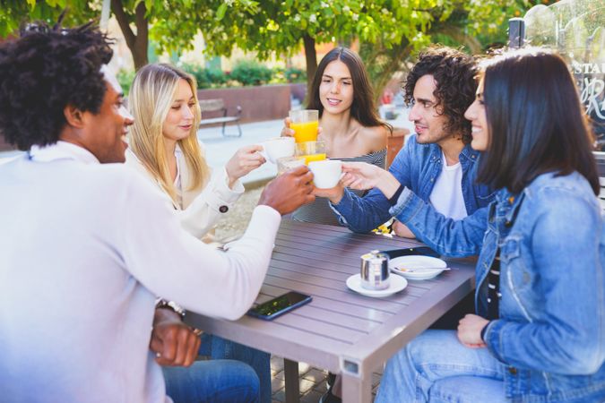 Men and women raising their juice and coffee in celebration at an outdoor restaurant